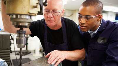 two people in protective eyewear look at a drill bit during a project